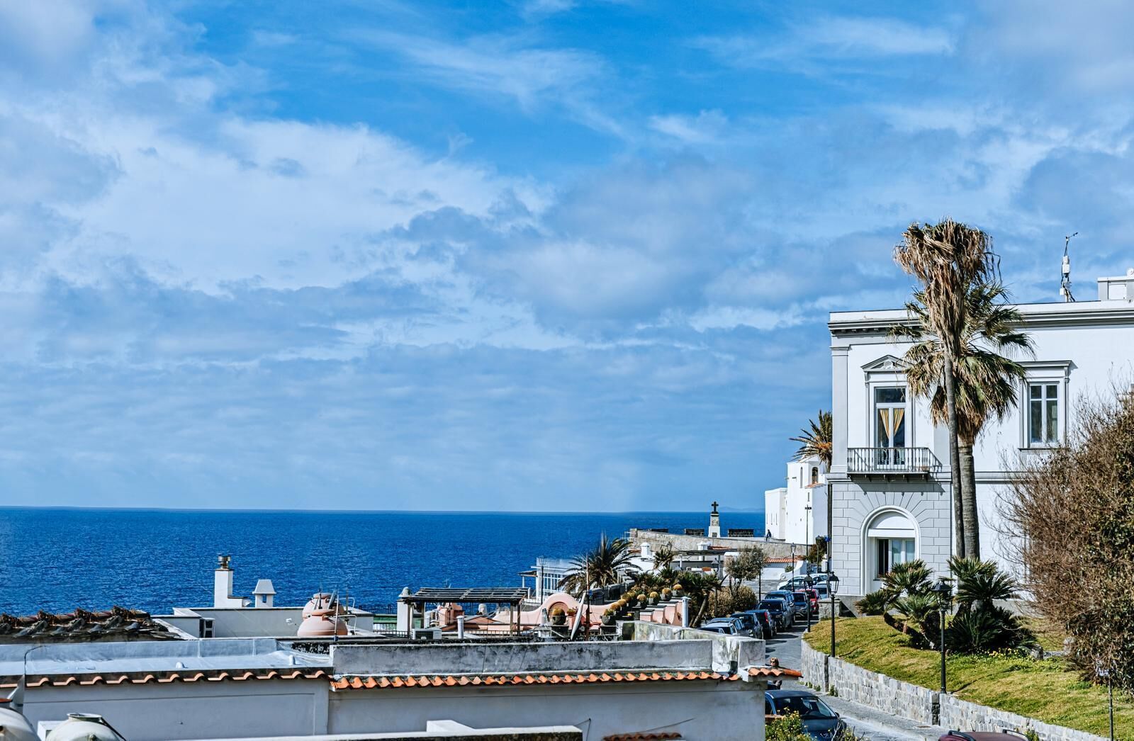 A coastal building with a view of the sea, a lighthouse, and a palm tree.