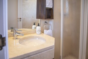 A bathroom with a beige marble sink, a modern faucet, a mirror, and a wooden cabinet above the mirror. - Calanova Golf Sensations Outdoor Vacations (Mijas Costa)