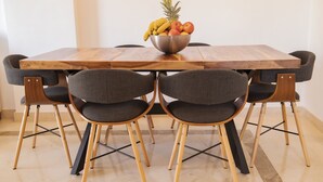 A wooden dining table with a fruit bowl, six grey upholstered chairs, and a tiled floor. - Alfresco Stays Calanova Golf Sensations (Mijas Costa)