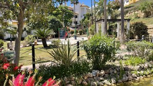 A landscaped garden with a pond, palm trees, and a playground. - Alfresco Stays Calanova Golf Sensations (Mijas Costa)