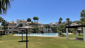 A pool area with a thatched gazebo, palm trees, and a clear blue sky. - Alfresco Stays Calanova Golf Sensations (Mijas Costa)