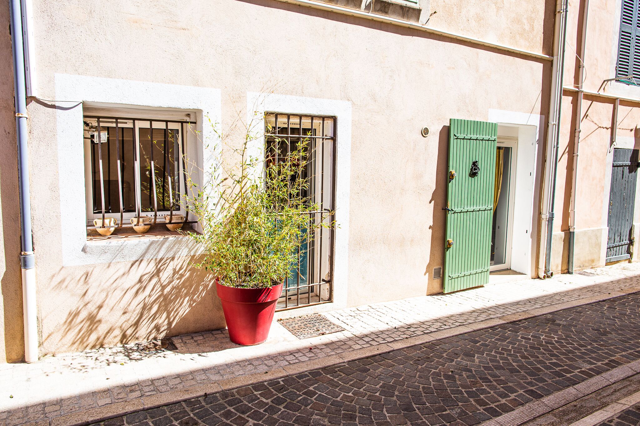 Un bâtiment devant lequel se trouve une fenêtre ornée d’une grille métallique et sur laquelle est posée une plante en pot.