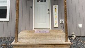 Ein Haus mit weißer Haustür, einer kleinen Veranda mit Holzsäulen und einem Willkommen-Schild.