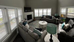 Ein Wohnzimmer mit Kamin, Deckenventilator und großem Fenster mit Jalousien.