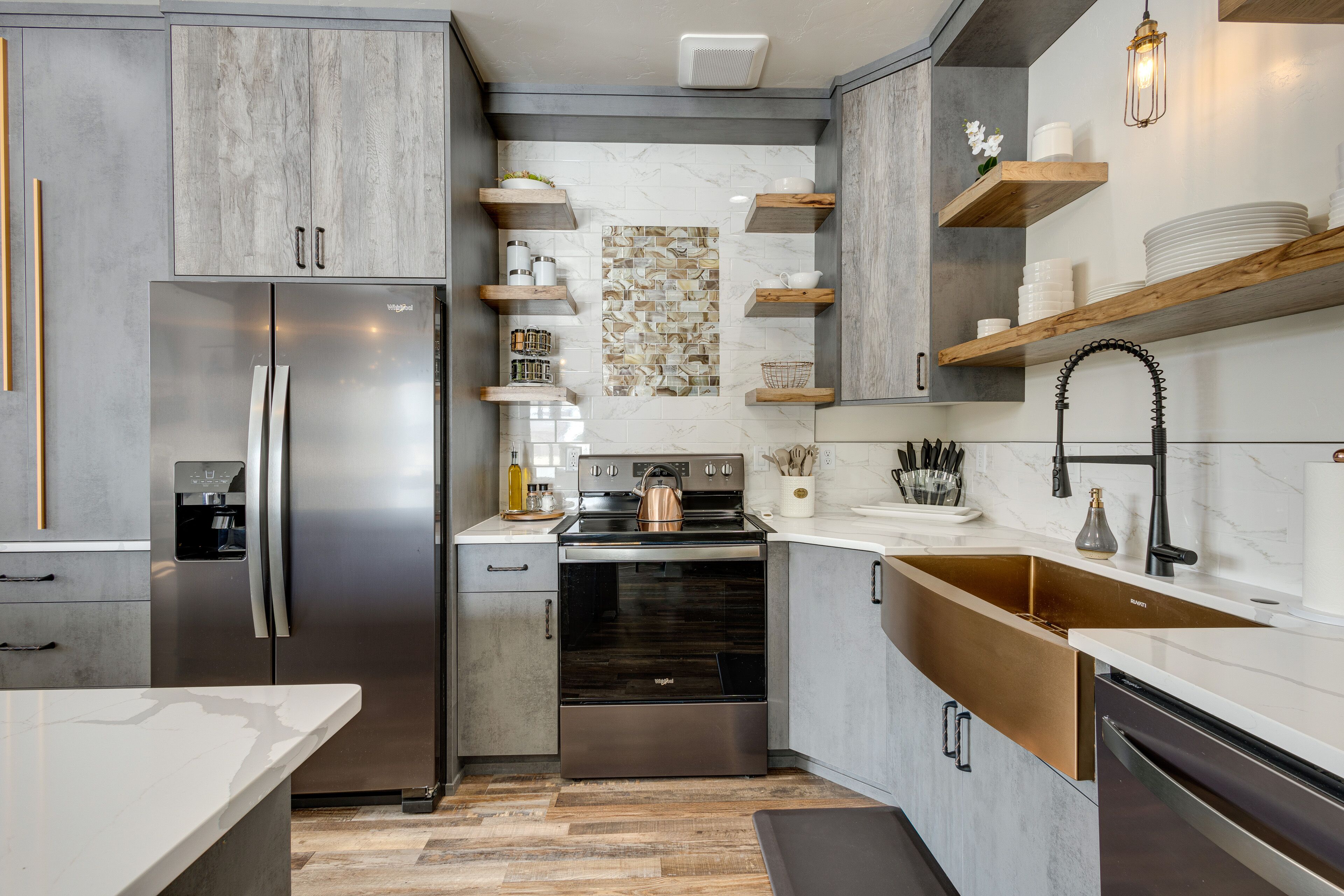 Een moderne keuken met een koelkast, oven en vaatwasser van roestvrij staal, houten planken en een marmeren achterwand.