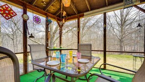 Un espacio de comedor al aire libre cubierto con una mesa de vidrio, sillas y vistas a árboles.