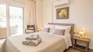 Una habitación de hotel con cama, una silla, una mesita de noche con lámpara, aire acondicionado y un cuadro en la pared.