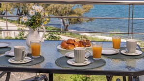 Una mesa con alimentos para el desayuno y un florero, con vistas a la costa.
