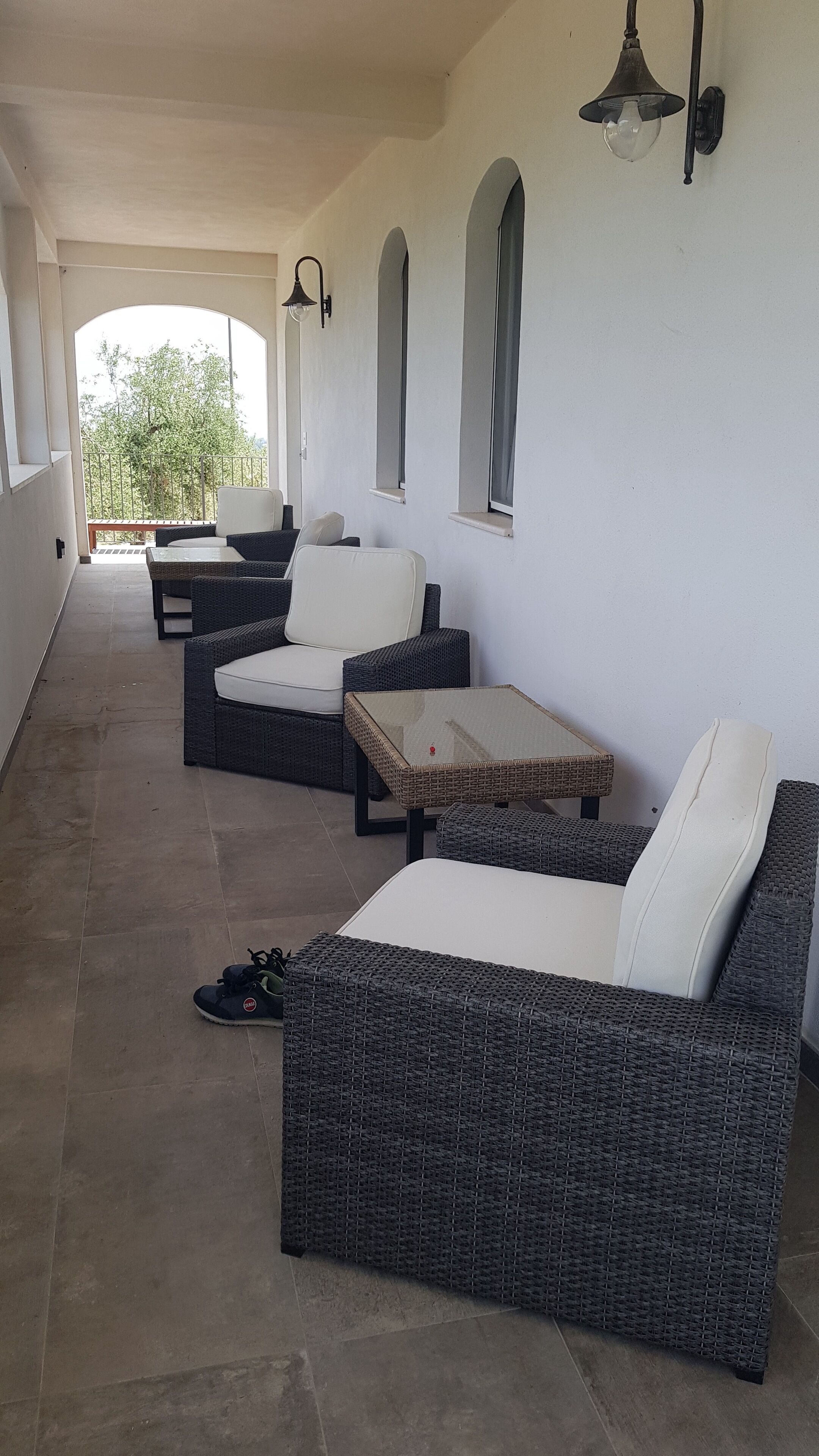 A covered outdoor seating area with wicker furniture, a glass-top table, and wall-mounted lighting.