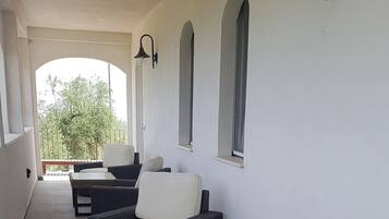 A covered outdoor seating area with wicker furniture, a glass-top table, and wall-mounted lighting.
