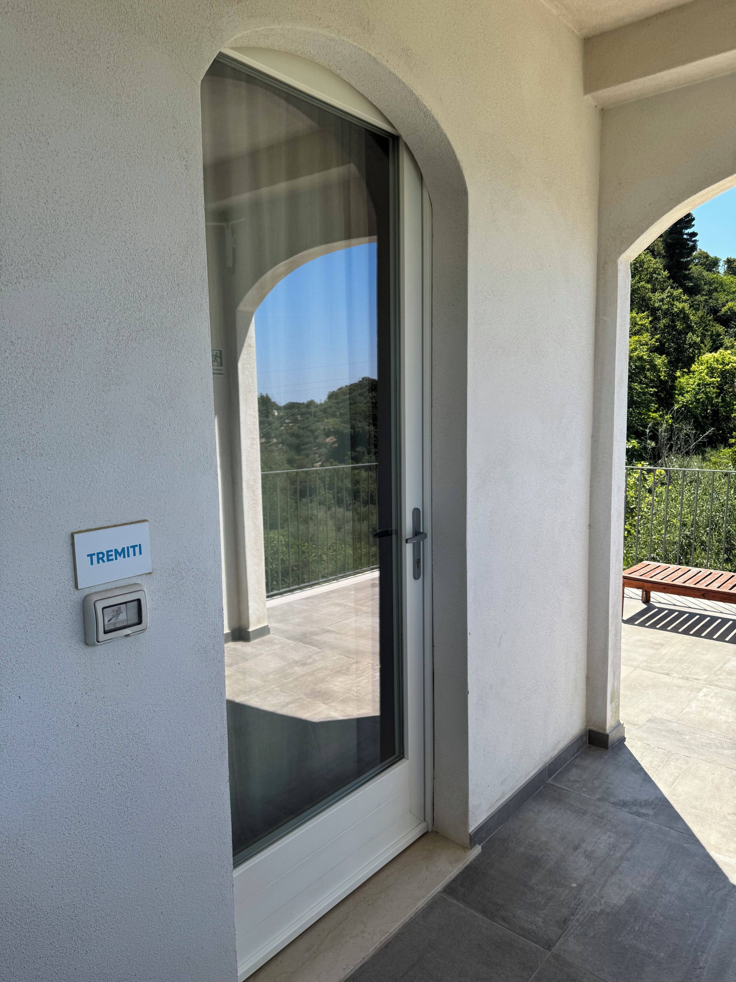 A modern building entrance with a glass door, a sign reading "TREMITI", and a small electronic device mounted on the wall.