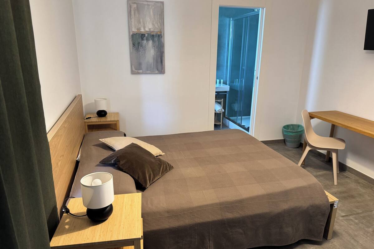 Ein Schlafzimmer mit Bett, Nachttisch, Lampe, Stuhl und einem Bild an der Wand.