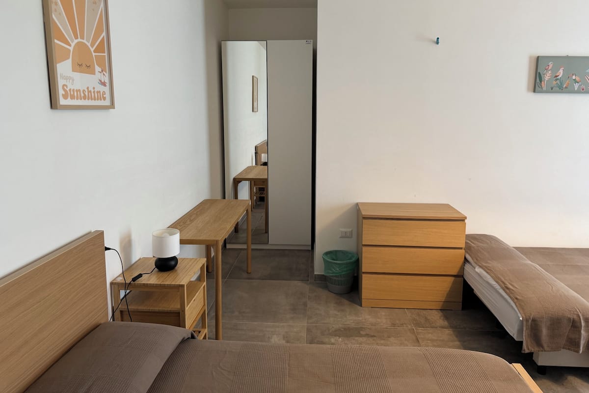 Ein Schlafzimmer mit zwei Betten, einem Holztisch, einem Stuhl, einer Kommode und einem an der Wand hängenden Bild.