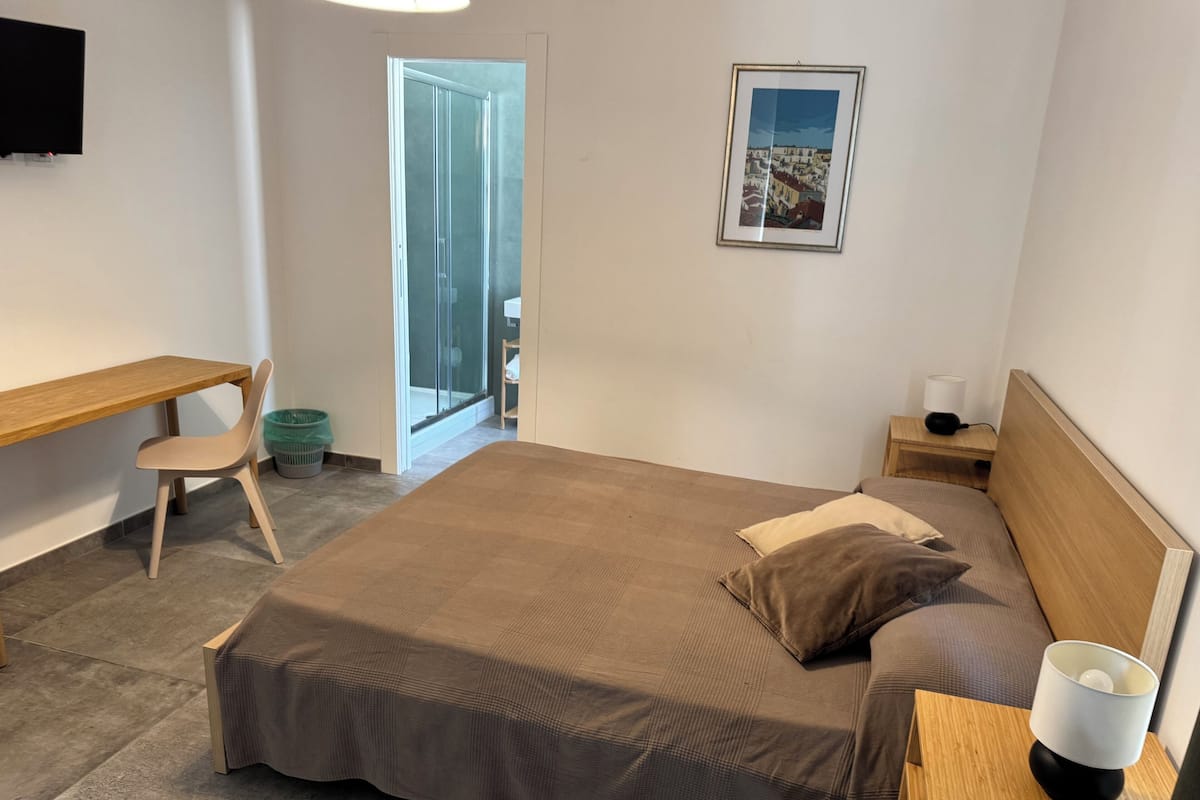 Ein Schlafzimmer mit Bett, Schreibtisch, Stuhl, Nachttisch, Lampe und einem gerahmten Bild an der Wand.