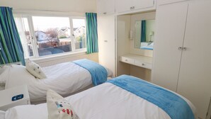 A hotel room with two beds, a window with curtains, a bedside table, a mirror, and a wardrobe.