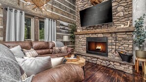 A cozy living room with a stone fireplace, leather sofa, and a flat-screen TV mounted on the wall.
