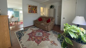 Un salon avec un canapé beige, un tapis coloré, une plante en pot et un tableau accroché au mur.