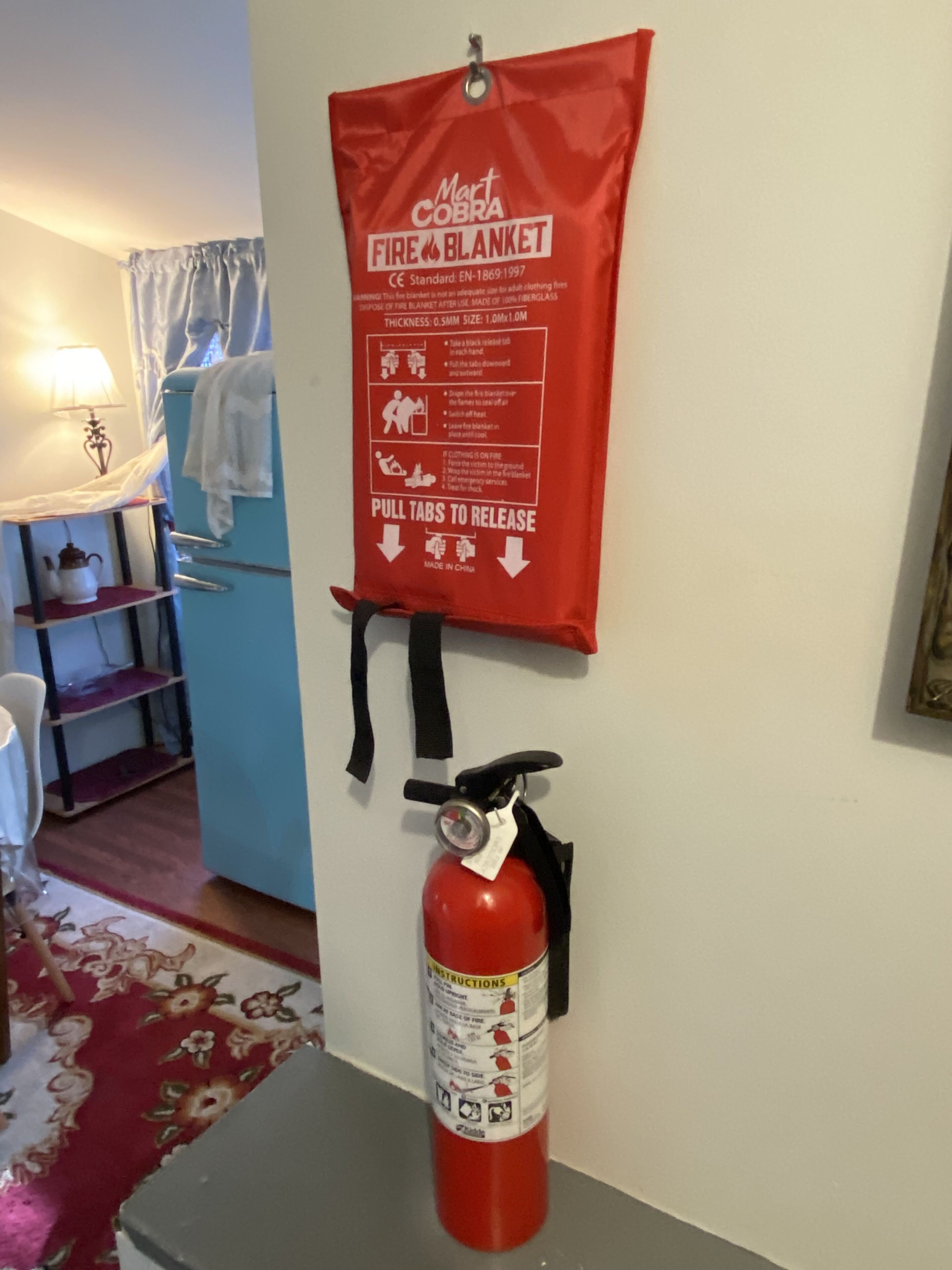 A fire blanket hanging on a wall with instructions, and a fire extinguisher below it.