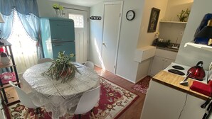 Une cuisine compacte équipée d’un réfrigérateur, d’une cuisinière et d’un évier. Une table à manger avec des chaises et un tapis à motifs floraux se trouvent au premier plan.