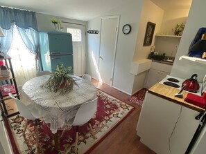 Une cuisine compacte équipée d’un réfrigérateur, d’une cuisinière et d’un évier. Une table à manger avec des chaises et un tapis à motifs floraux se trouvent au premier plan.