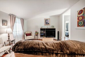 A bedroom with a large bed, a chair, a desk, a bookshelf, and a television.