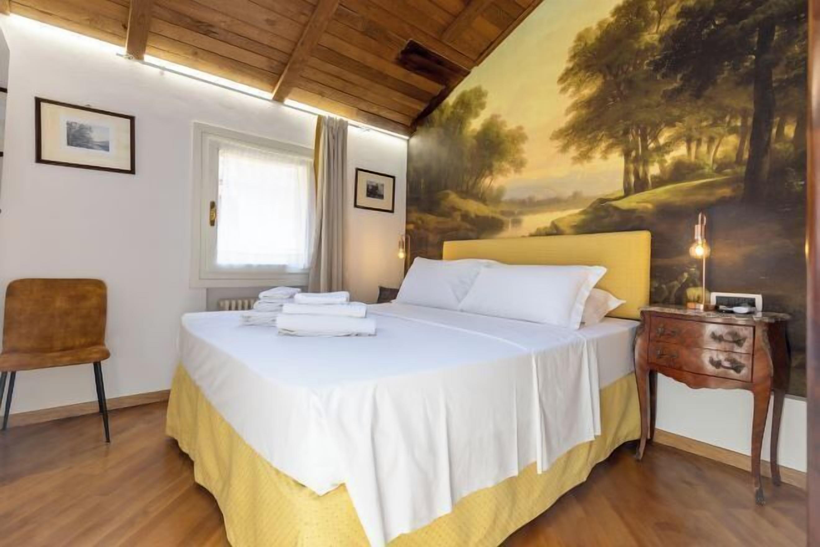 A bedroom with a bed, a chair, a nightstand, and a mural on the wall.