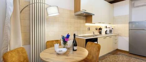 A modern kitchen with white cabinets, a stainless steel refrigerator, and a round wooden table with chairs.