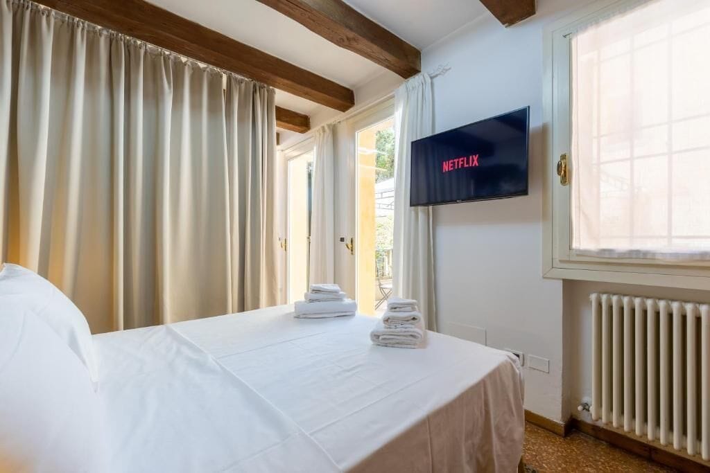 Une chambre d’hôtel avec un lit, un téléviseur fixé au mur, une fenêtre avec des rideaux et un radiateur.