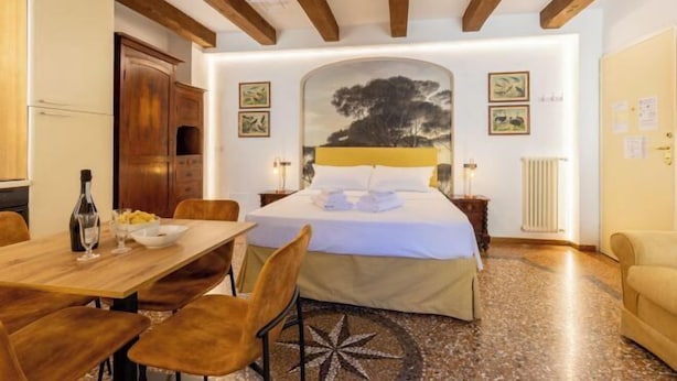 A hotel room with a bed, a dining table, chairs, a wooden cabinet, and a radiator. - Bolognaroomscom - Frassinago deluxe (Bologna)