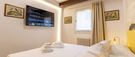 Quarto de hotel com uma cama, televisão de tela plana na parede e uma janela com cortinas.