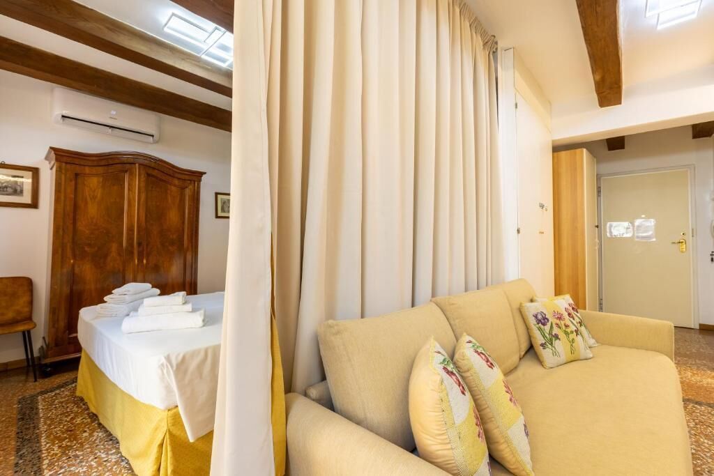 A hotel room with a bed, a sofa, a wooden wardrobe, and a door.