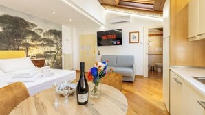 A modern hotel room with a bed, a round dining table with wine glasses and a bottle, a TV displaying Netflix, and a view of the outdoors. - Bolognaroomscom - Frassinago deluxe (Bologna)