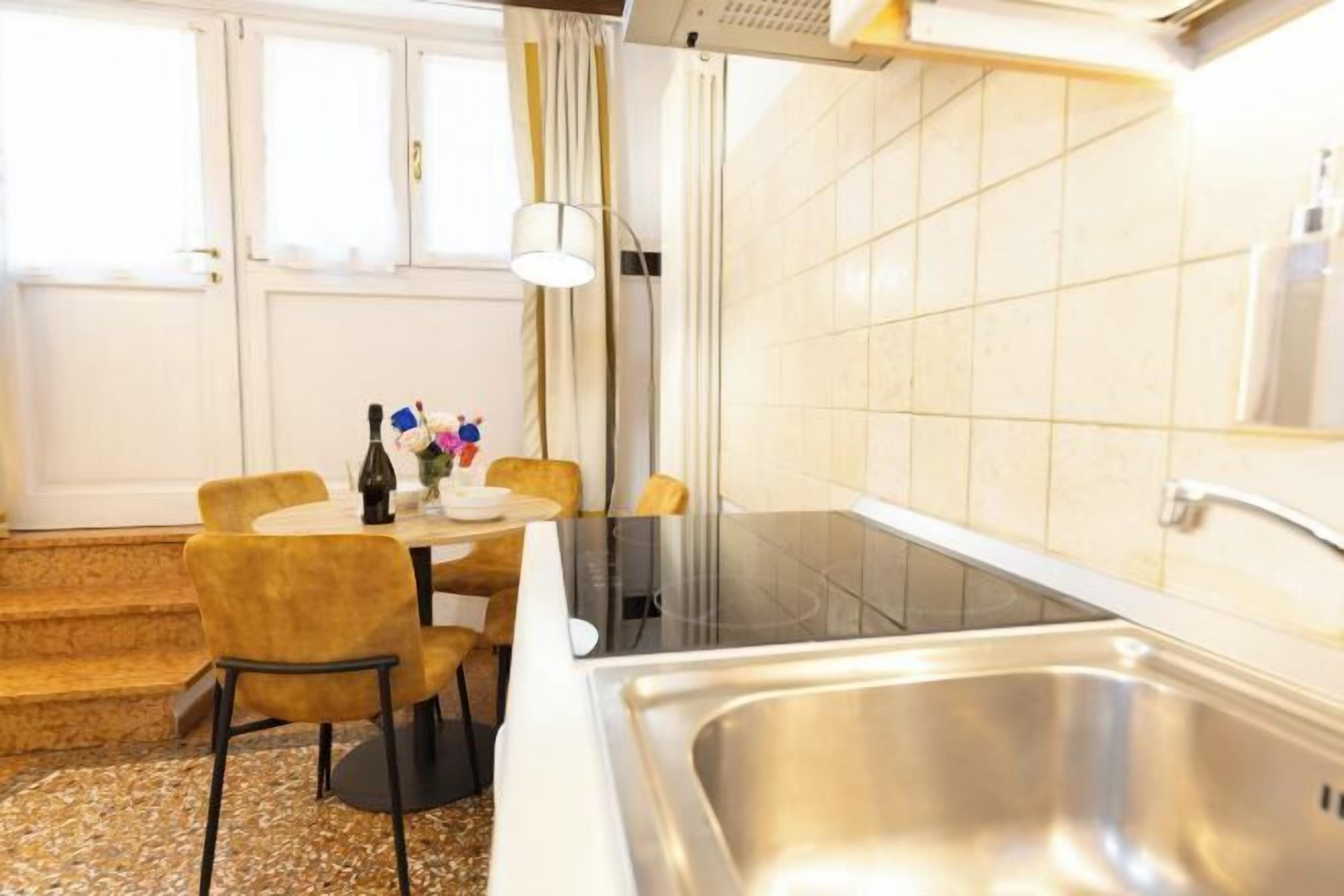 Une cuisine de taille réduite, équipée d’un évier, d’une table avec des chaises et d’une fenêtre avec des rideaux.