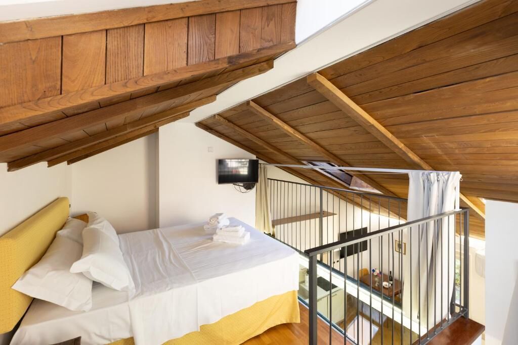 Ein Schlafzimmer mit einem Bett, Holzboden, einem Balkon mit Geländer und einem an der Wand montierten Fernseher.