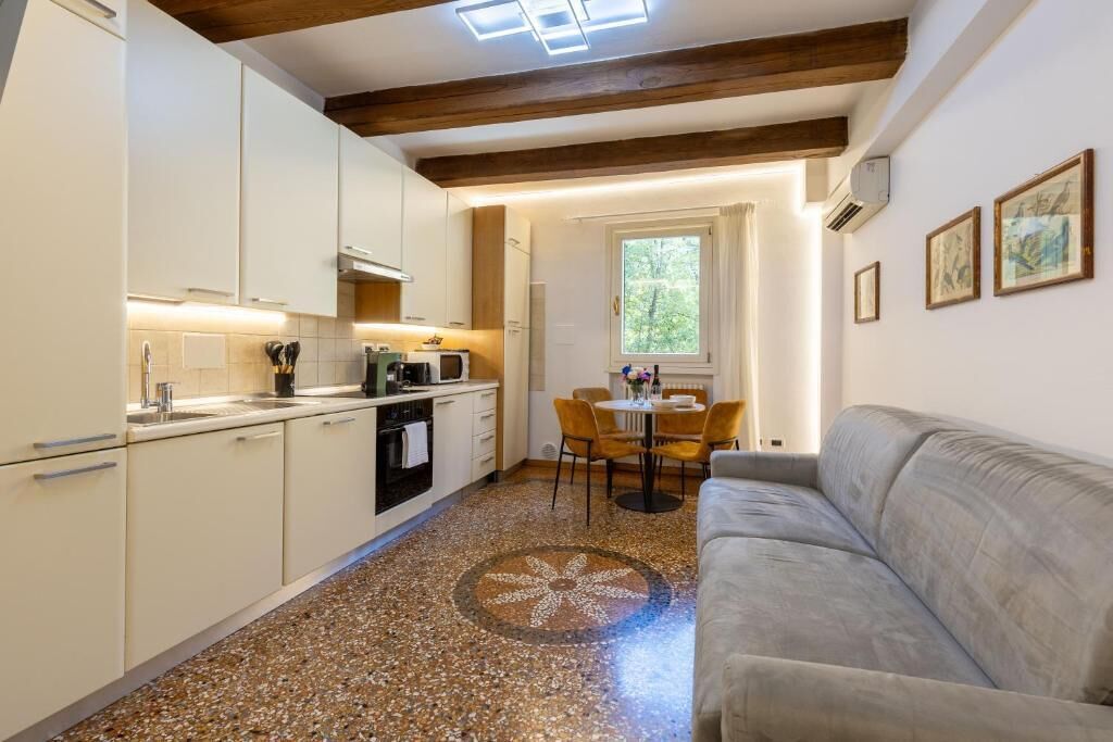 A compact kitchen with white cabinets, a dining area with a round table and chairs, and a gray sofa in a living area.