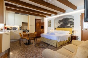 Habitación de hotel compacta con cama, sofá, zona de comedor con mesa y sillas, cocina y un cuadro grande en la pared.
