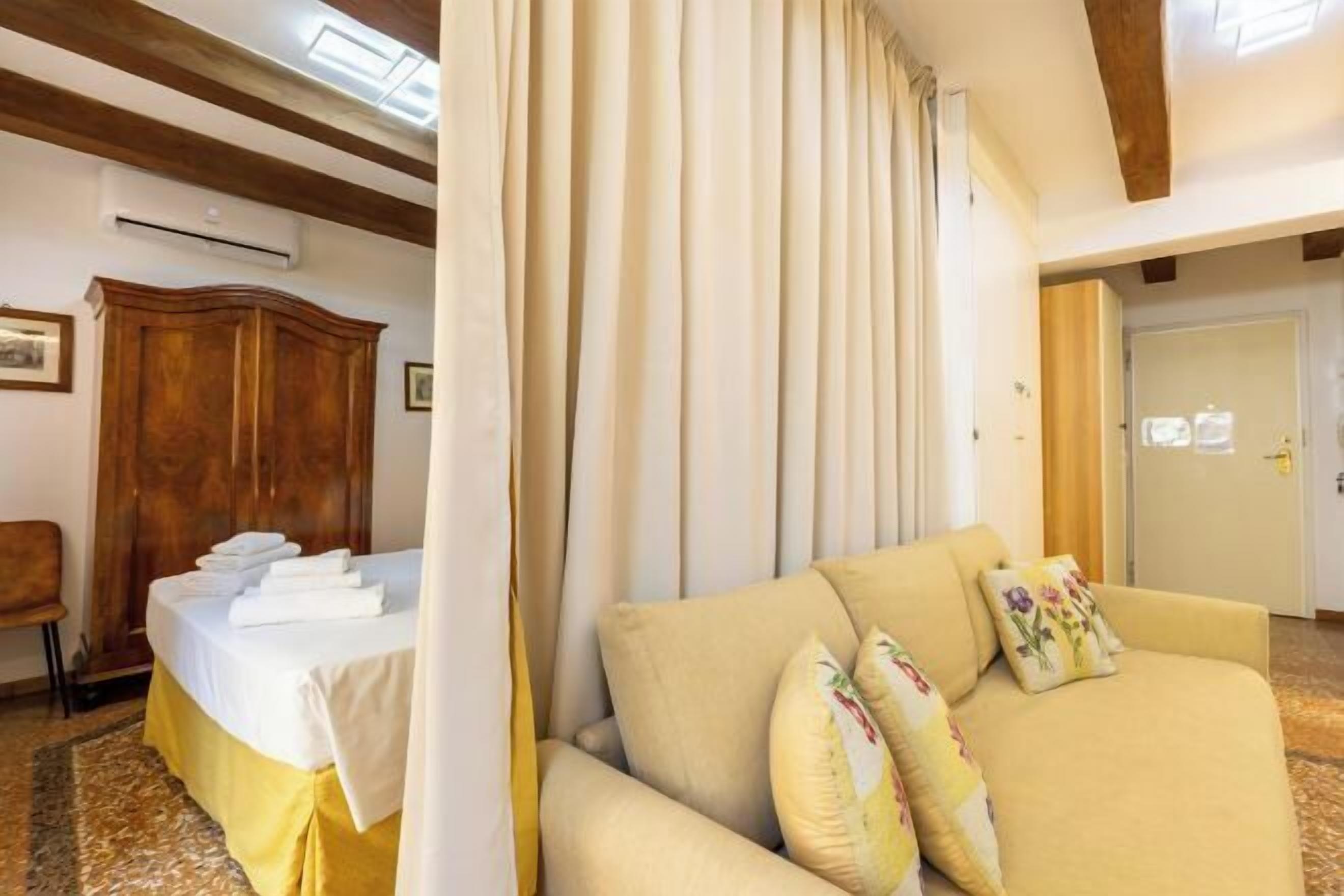 Una habitación de hotel con una cama, un sofá, un armario de madera y una cortina.