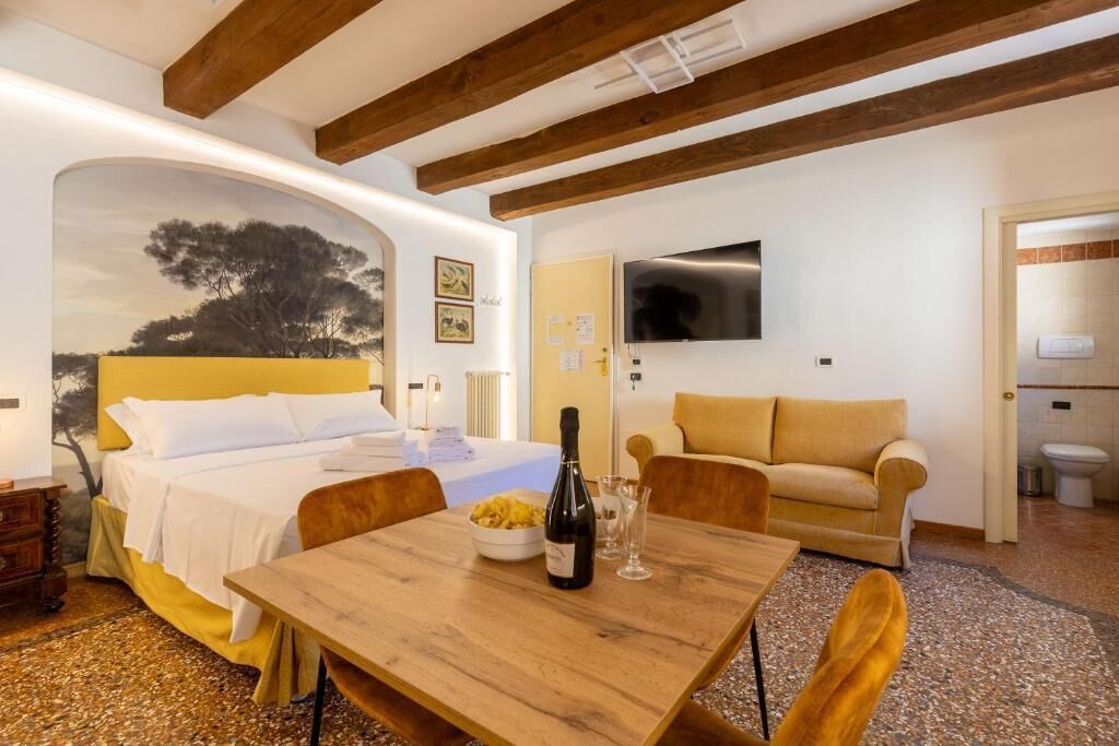 Un dormitorio con cama, una mesa de madera, una botella de vino y un televisor en la pared.