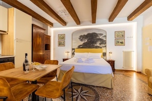 A bedroom with a bed, wooden ceiling beams, a dining table with chairs, and artwork on the walls. - Bolognaroomscom - Frassinago deluxe (Bologna)
