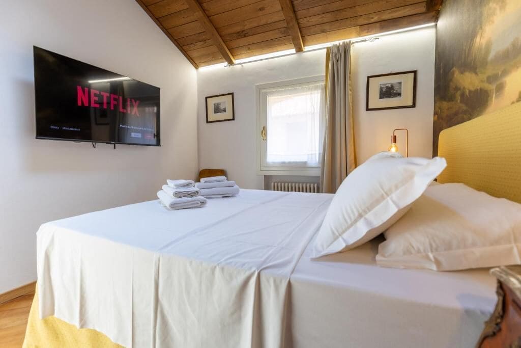 Ein Hotelzimmer mit Bett, Wandfernseher, Fenster mit Vorhängen und Heizkörper.