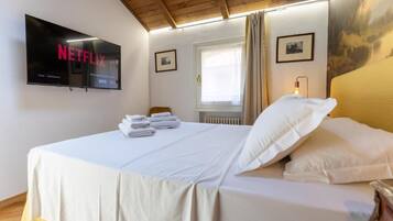 Ein Hotelzimmer mit Bett, Wandfernseher, Fenster mit Vorhängen und Heizkörper.