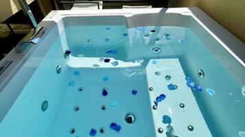 A hot tub with blue pebbles and a white lounge chair.