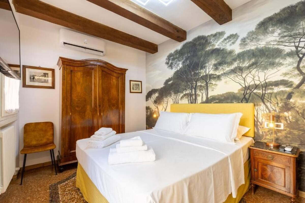 A bedroom with a bed, wooden wardrobe, and a mural of trees.