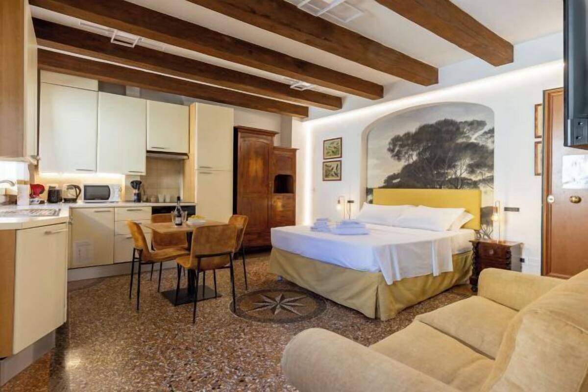 A compact hotel room with a bed, a sofa, a dining area with a table and chairs, and a kitchen.