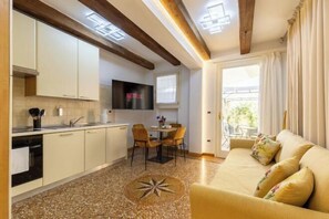 Una cocina moderna con armarios blancos, un comedor con mesa y sillas, un sofá con cojines estampados y un amplio ventanal con cortinas.