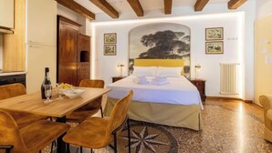A hotel room with a bed, a dining table with chairs, a kitchen area, and artwork on the walls. - Bolognaroomscom - Frassinago deluxe (Bologna)
