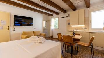 A hotel room with a bed, a dining area with chairs, a TV mounted on the wall, and a kitchen area.