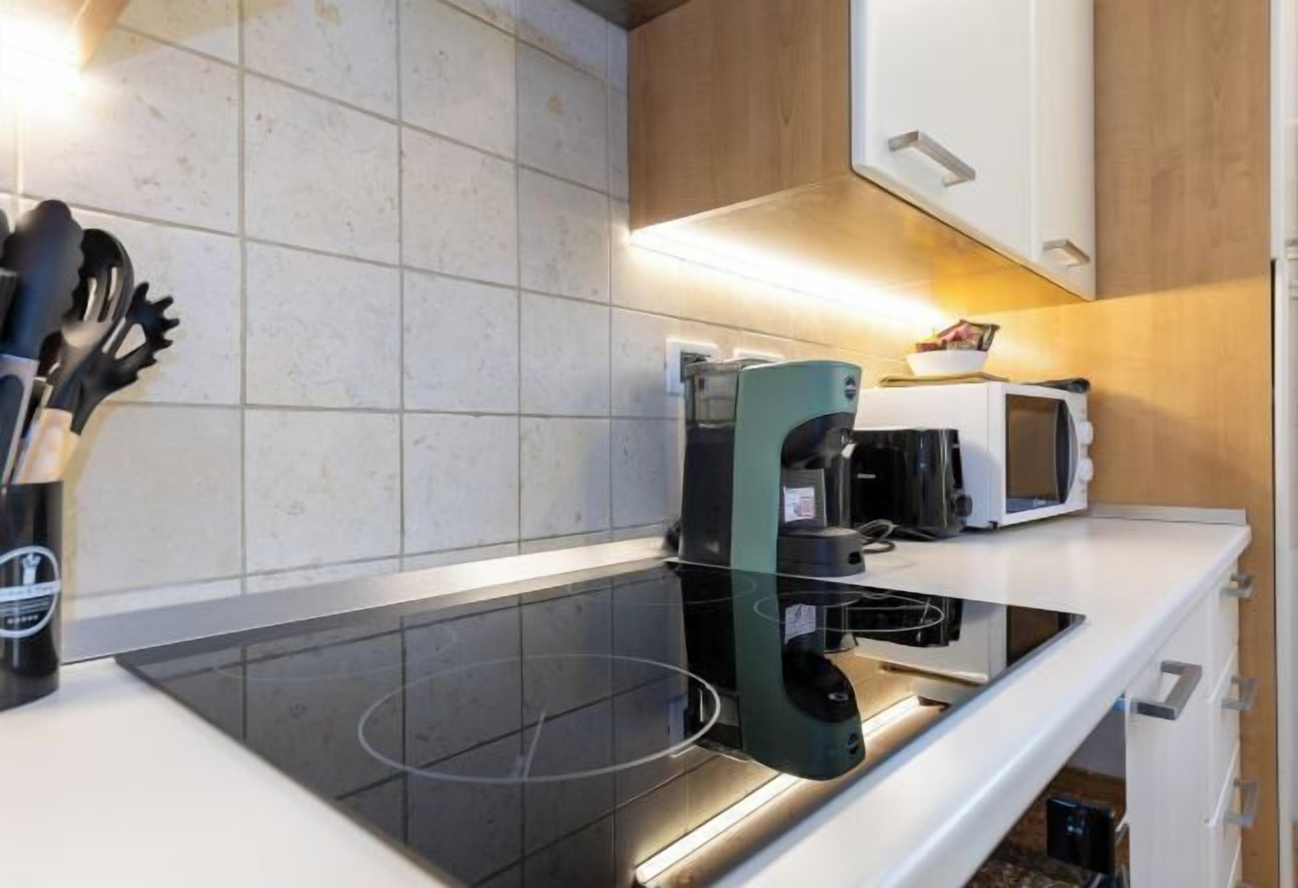 Une cuisine moderne équipée d’une plaque de cuisson à induction noire, d’un four à micro-ondes et d’une bouilloire.