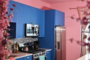 A kitchen with blue cabinets, a stainless steel microwave, a gas stove, and a refrigerator.