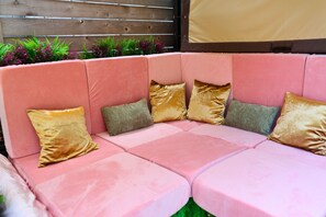 A pink sectional sofa with multiple cushions in a covered outdoor area.
